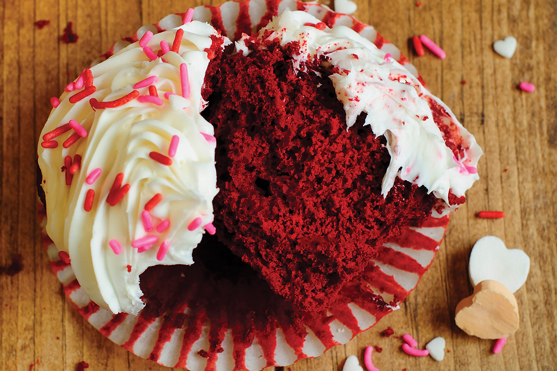 A red velvet cannellini bean cupcake split in half sitting on a cupcake wrapper