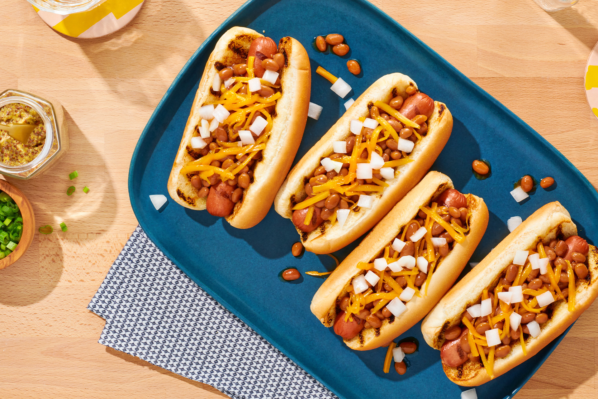 Four hot dogs with cheese, baked beans and onions on blue platter