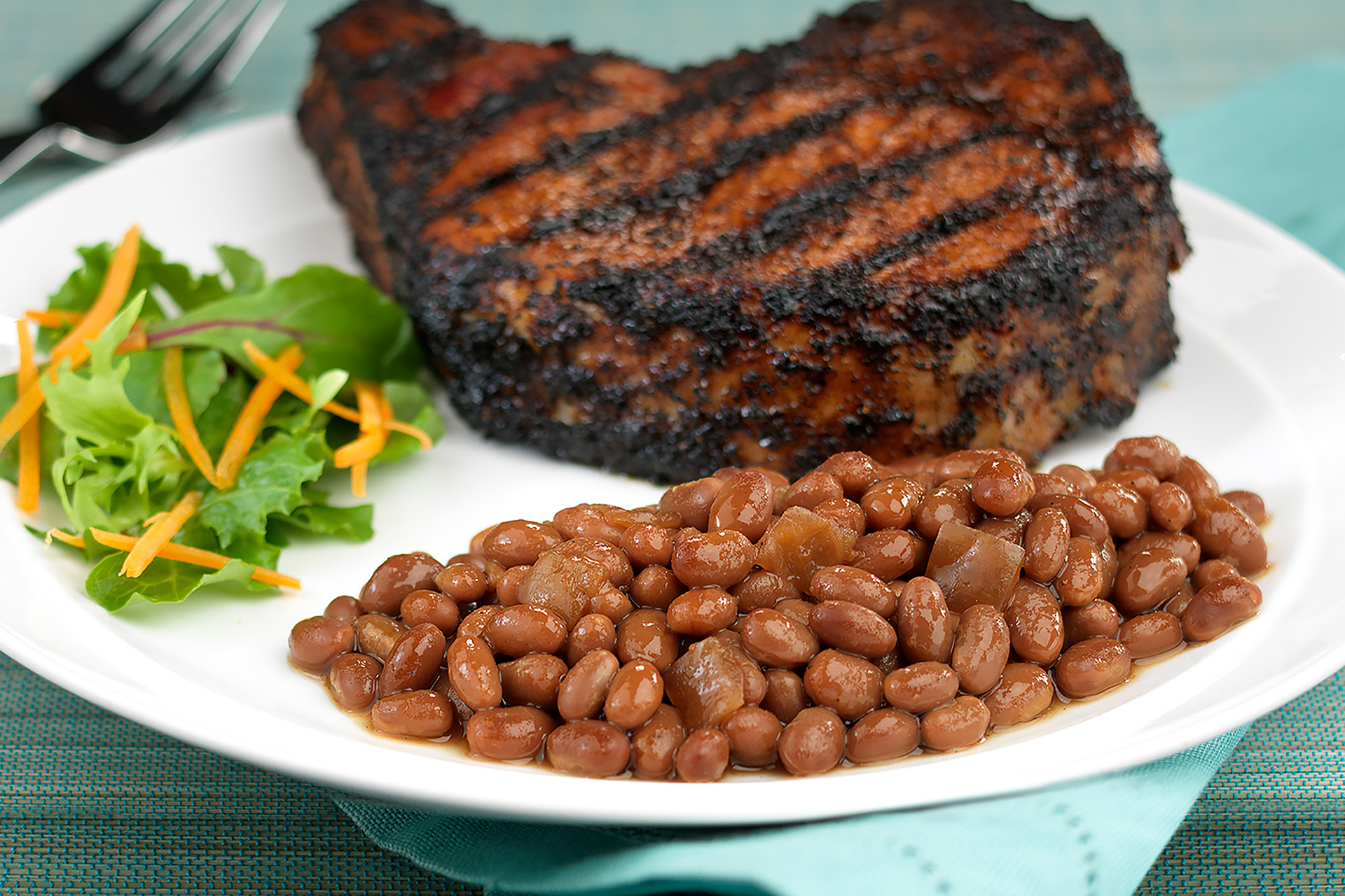 Coffee and chili rubbed pork chop with side of baked beans on white plate