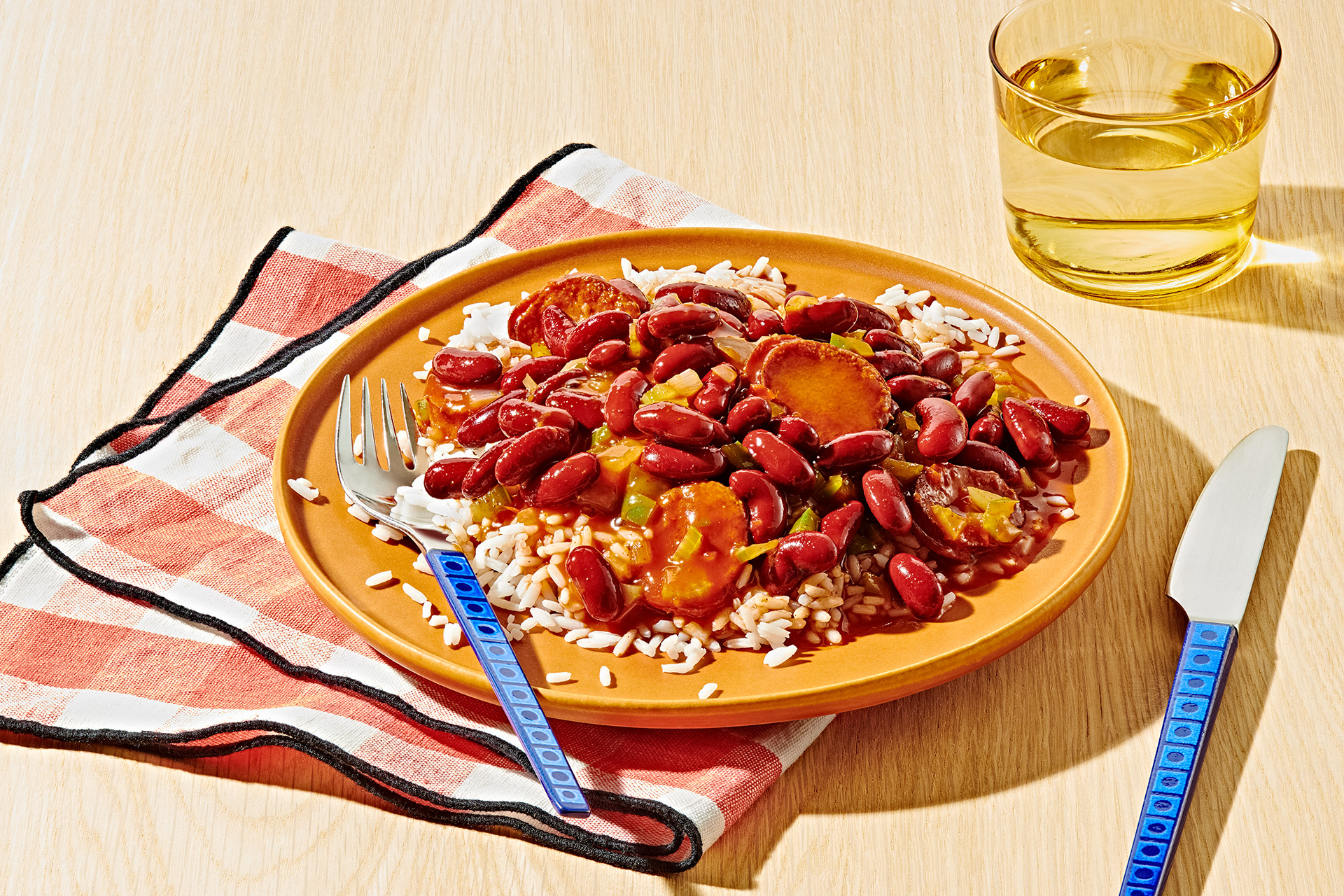 Red beans and rice with vegetables on a mustard colored plate with fork, knife, and a glass of water