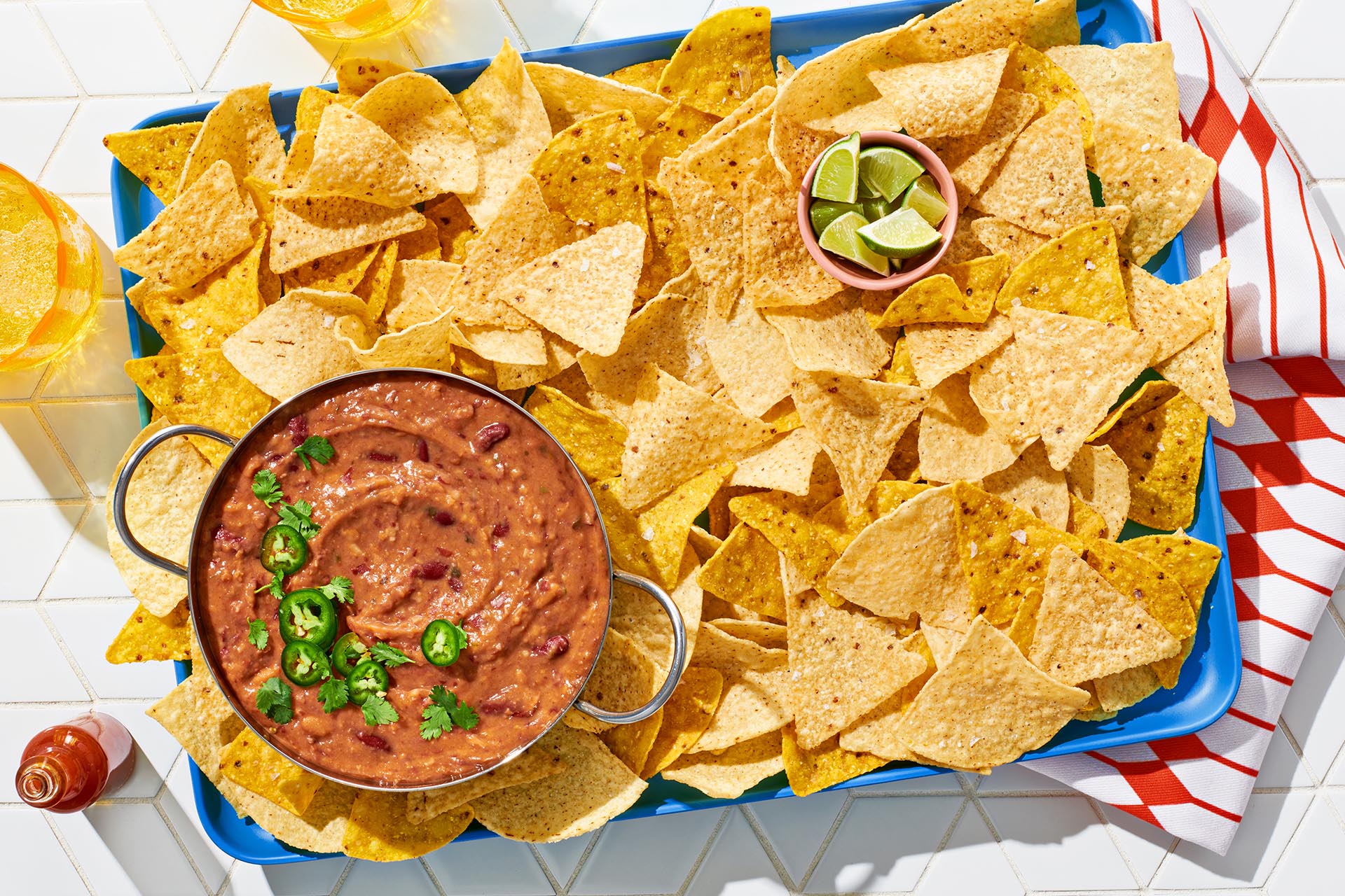 A bowl of half-smashed refried beans garnished with sliced jalapenos on a bed of tortilla chips