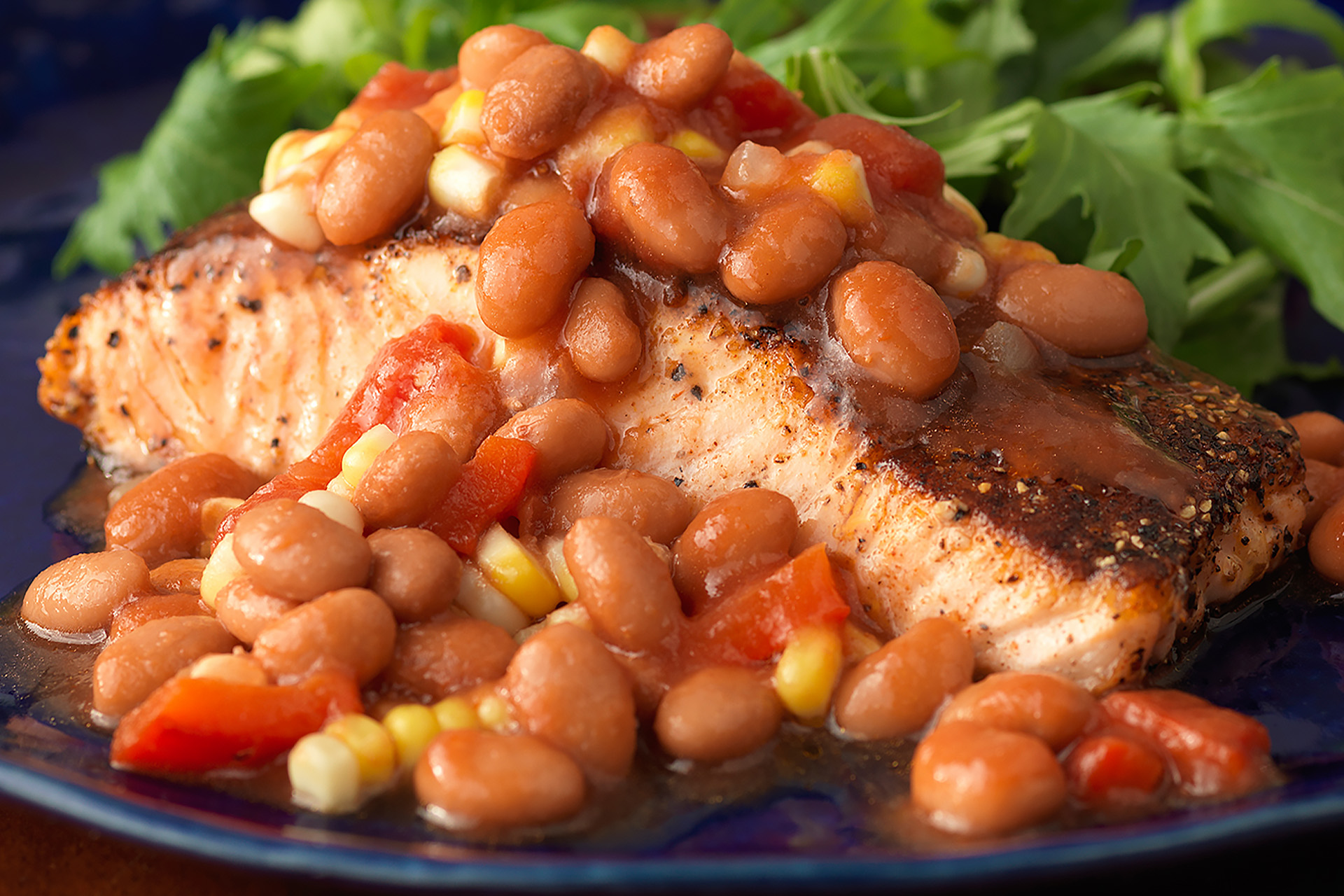 Pepper crusted salmon with pinto beans and greens on blue plate