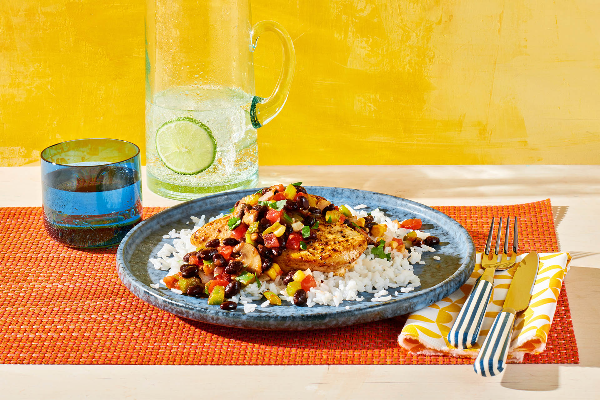 Salsa Chicken Skillet atop a bed of rice on an orange placemat with a pitcher of lime water.