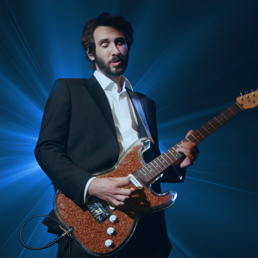 Josh Groban playing a guitar in front of a dark blue aura light burst