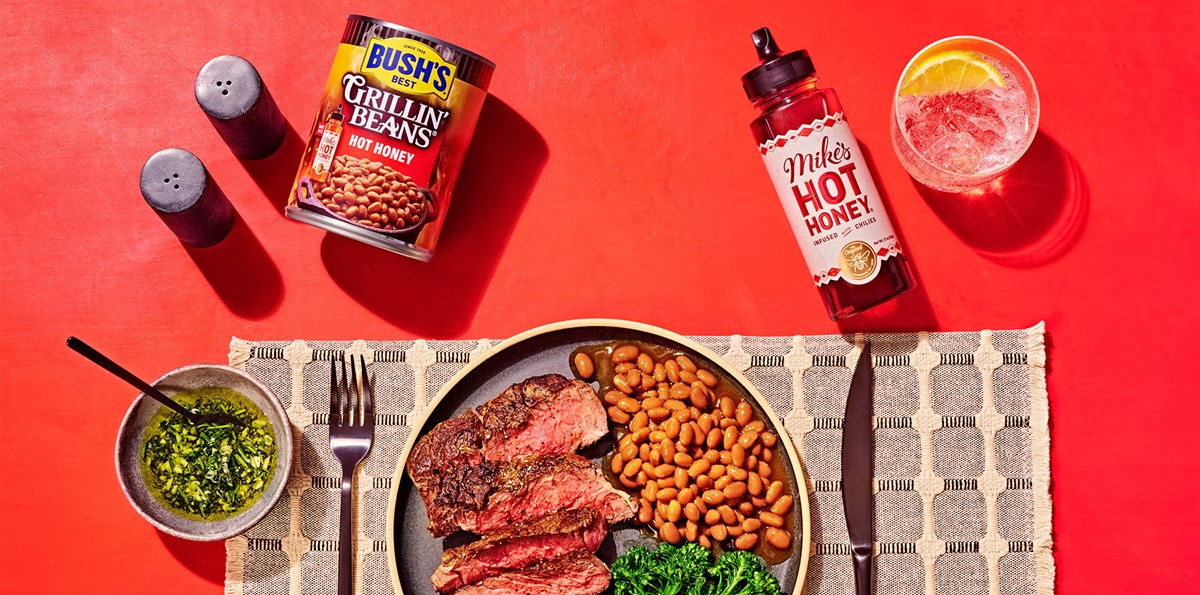 Plate with steak and beans on a table next to a can of Grillin' Beans and Mike's Hot Honey.