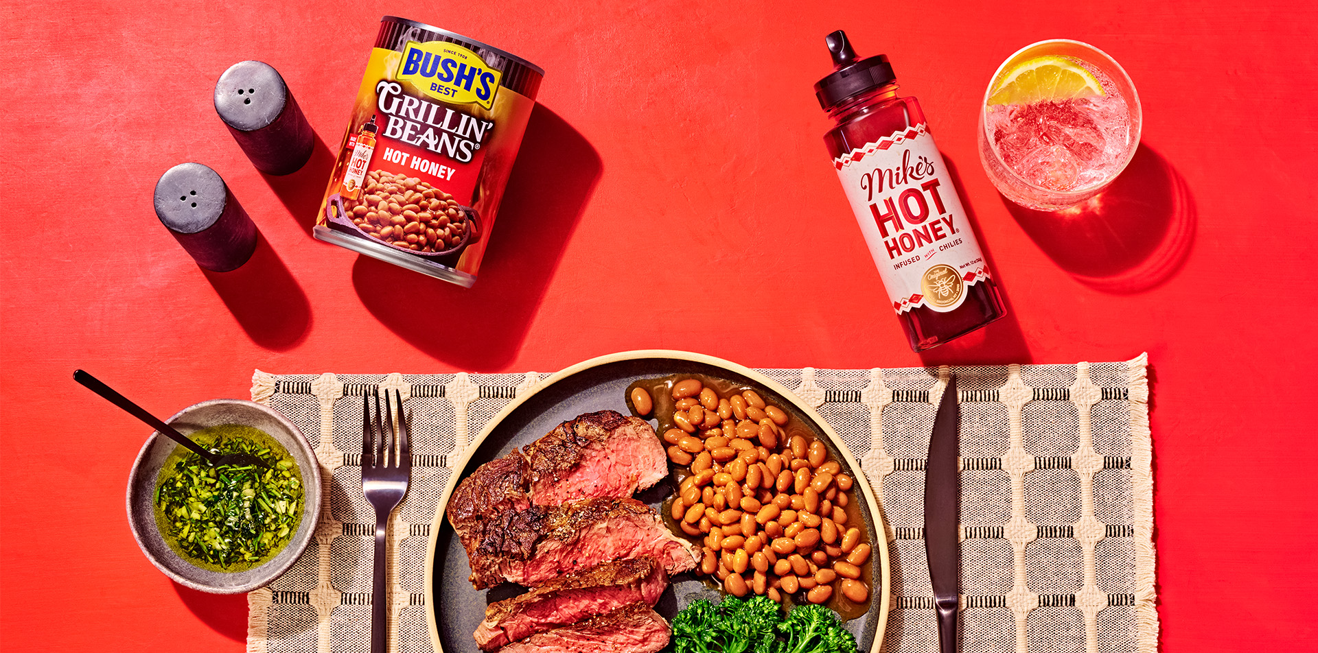 Plate with steak and beans on a table next to a can of Grillin' Beans and Mike's Hot Honey.