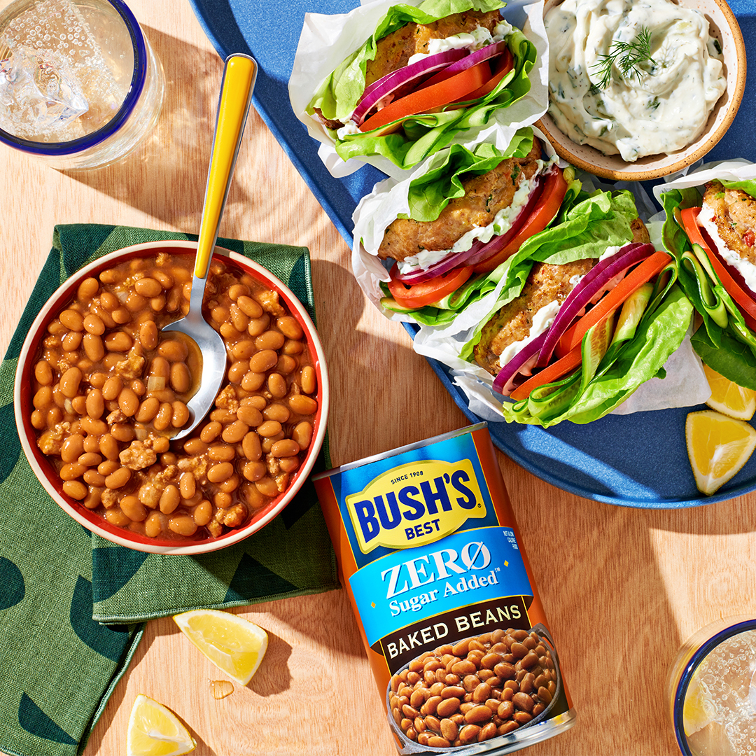 Can of Bush's Zero Sugar Added Baked Beans next to a bowl of baked beans and sandwiches.