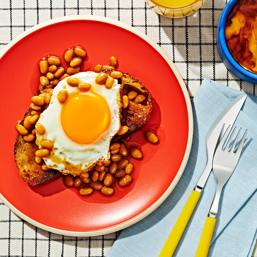 Baked Beans on Toast with a  fried egg on top, sitting on a red plate.