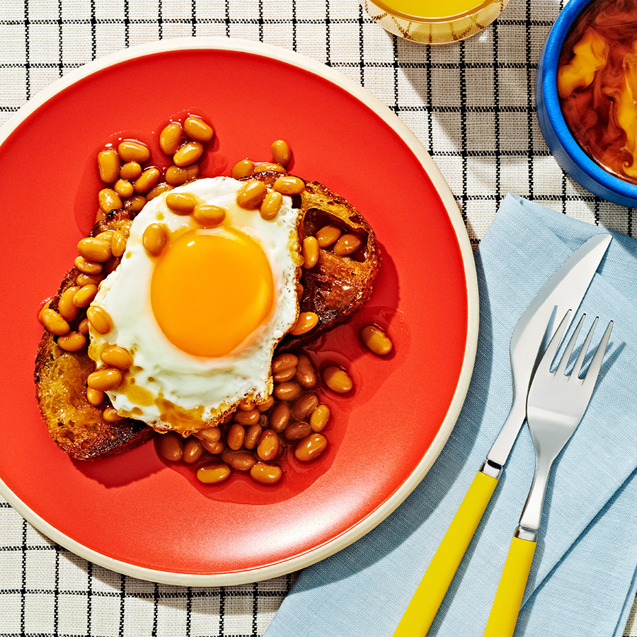 Baked Beans on Toast with a fried egg on top, sitting on a red plate.