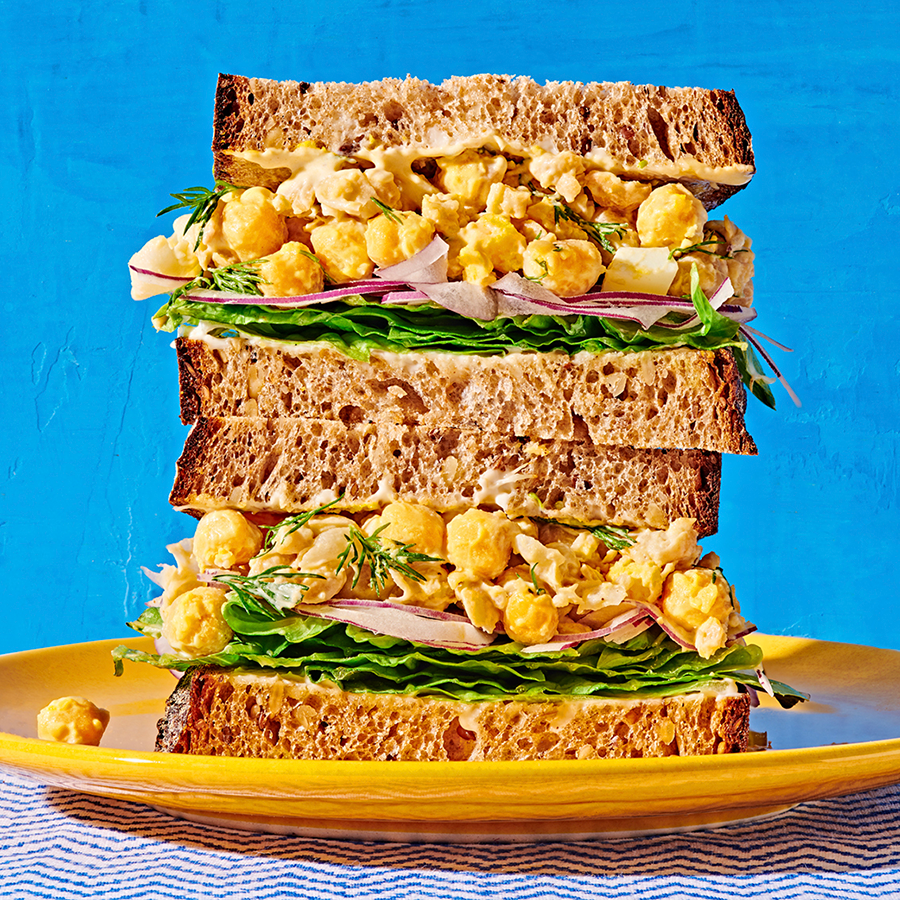 Tangy Chickpea Smash as the filling of a double decker sandwich sitting on a plate with a blue background.