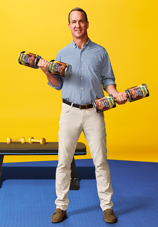 Peyton Manning doing arm curls with weights made of Bush's Zero Sugar Added Beans cans.