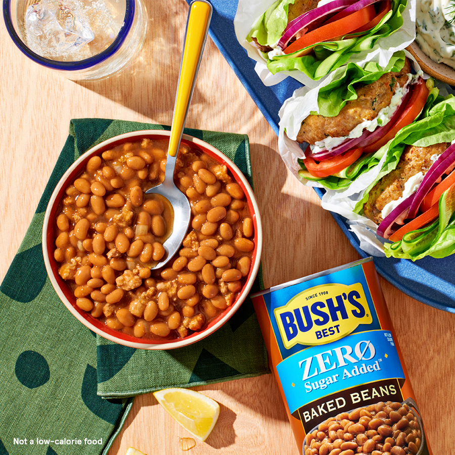a Bowl of baked beans next to a Bush's Zero Sugar Added Baked Beans can and a plate of  lettuce wraps.