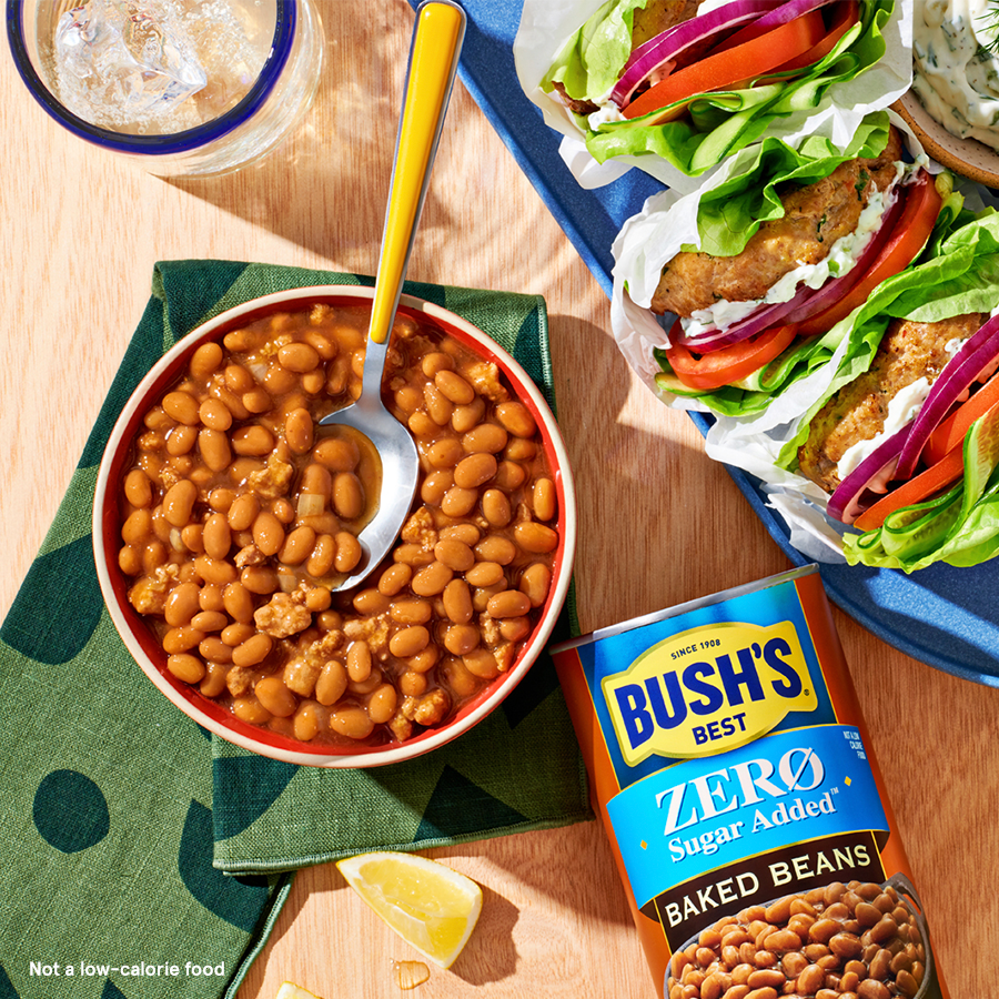 a Bowl of baked beans next to a Bush's Zero Sugar Added Baked Beans can and a plate of lettuce wraps.