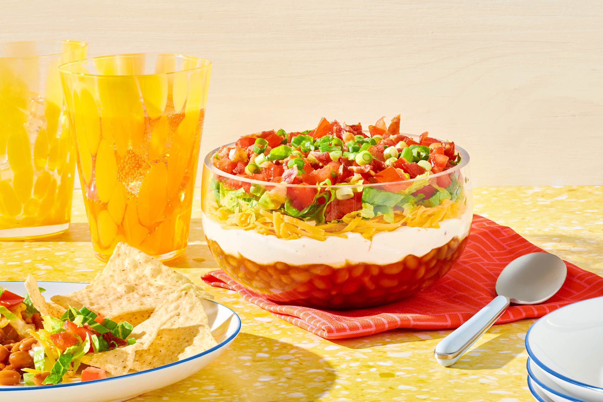 A bowl of layered bean dip on a red napkin next cups.