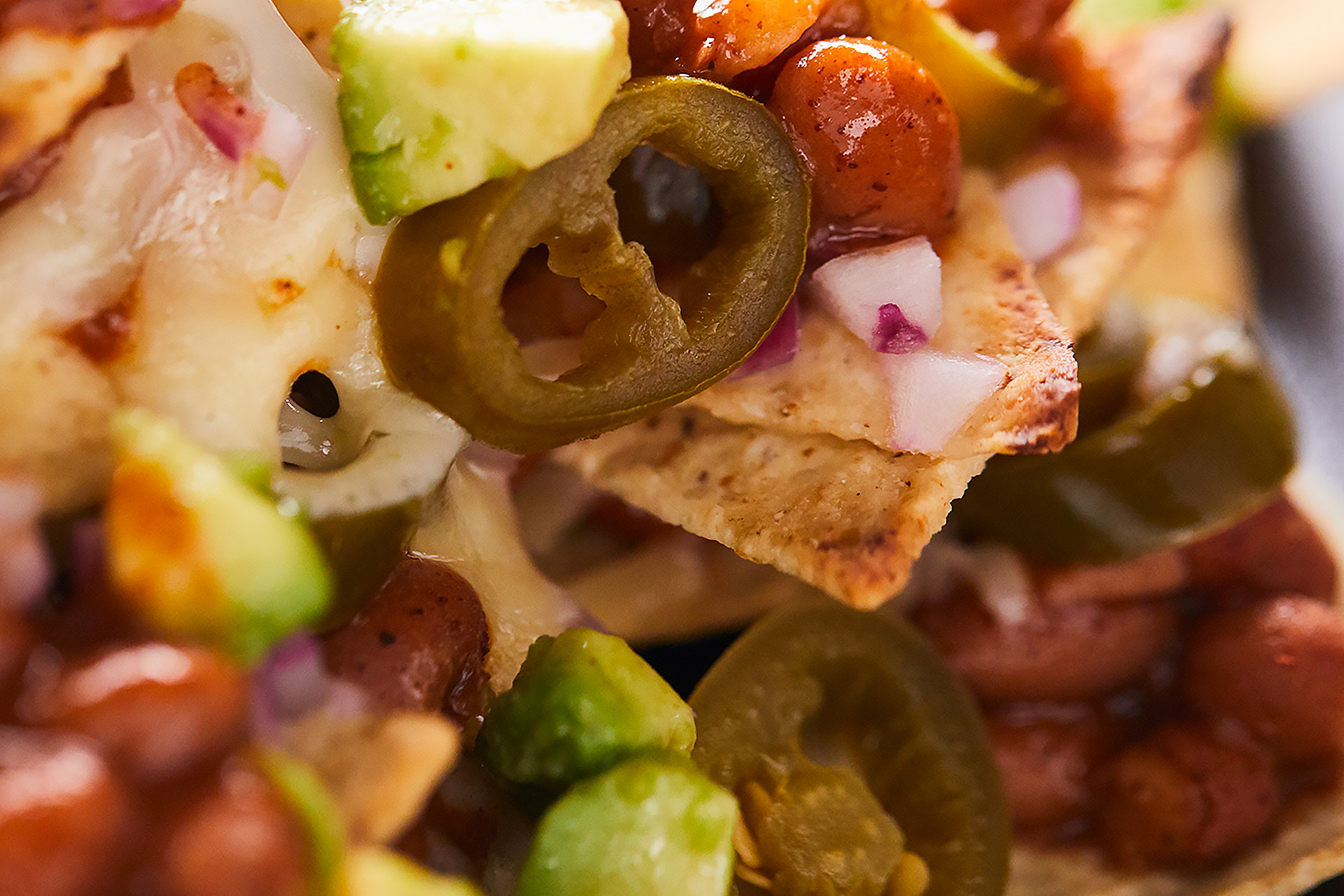An extreme close-up of nachos with melted cheese, beans and sliced jalapenos