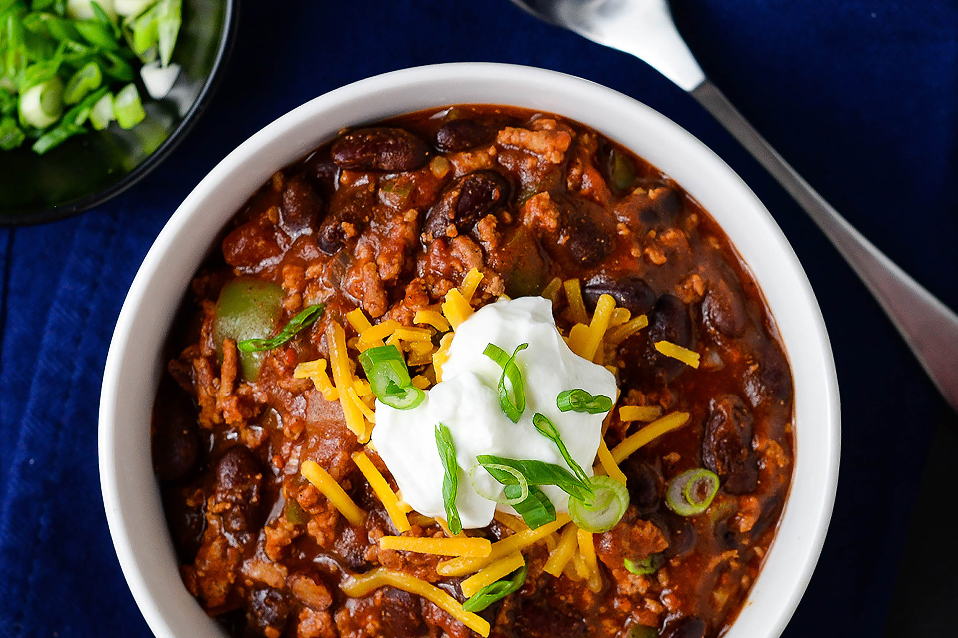 Beef and bean chili topped with sour cream and green onions in a white bowl