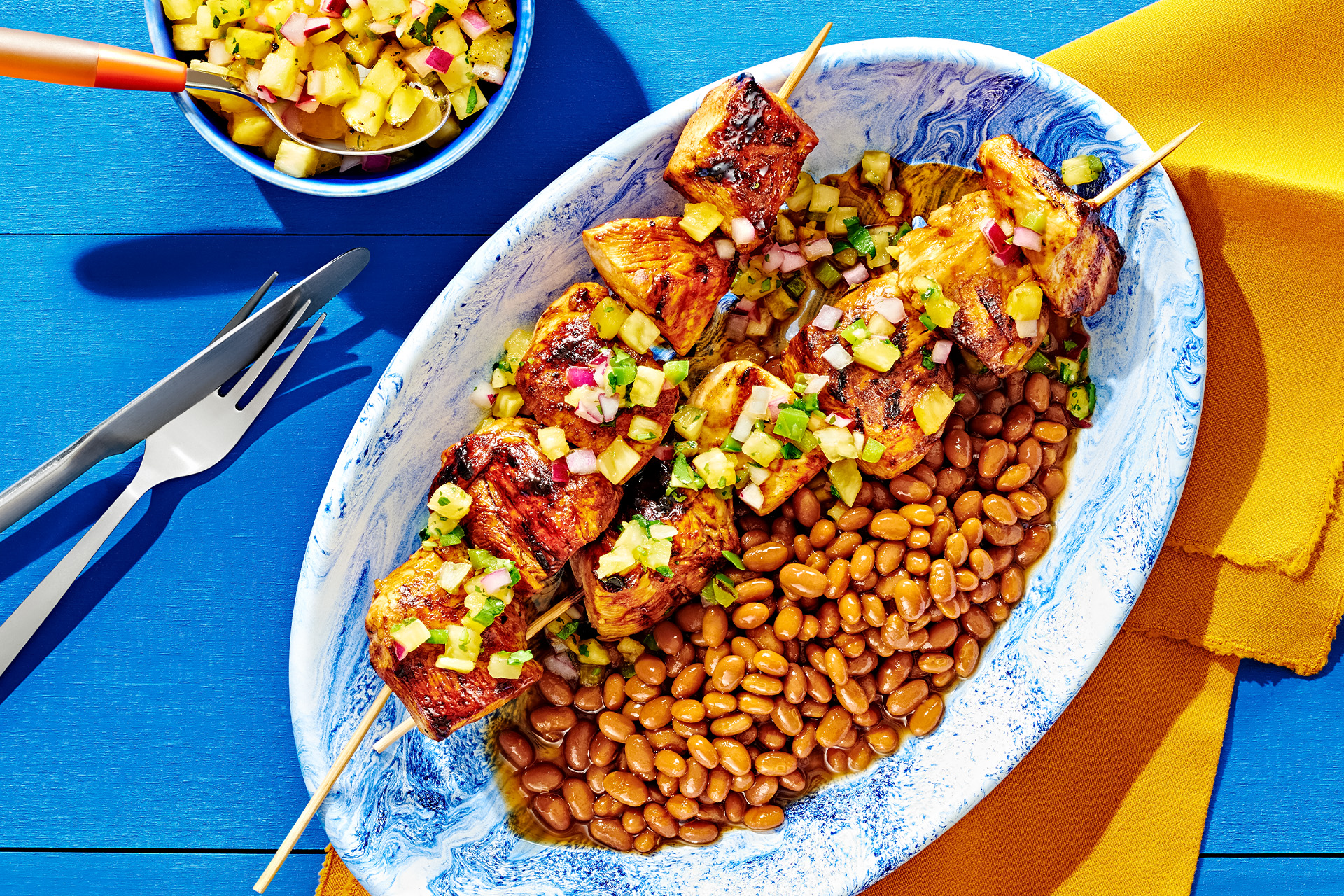 Grilled chicken skewers and baked beans on an oval blue and white swirl pattern plate
