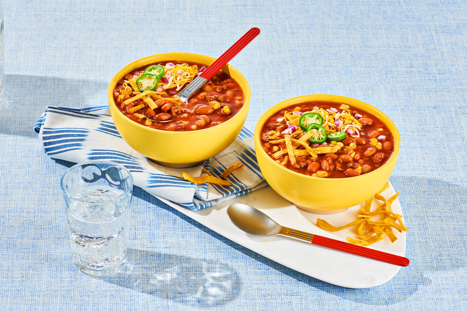 Two yellow bowls filled with Slow Cooker Taco Soup with fresh jalapeño, cheese and coupon toppings.