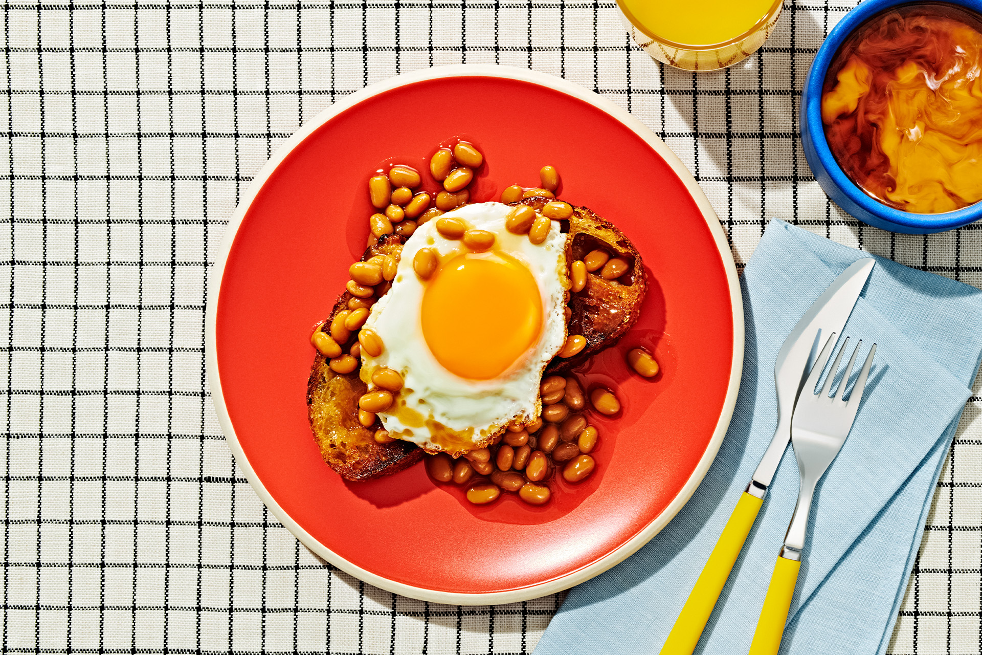 Sunny side up egg on a piece of toast covered in baked beans on a red plate
