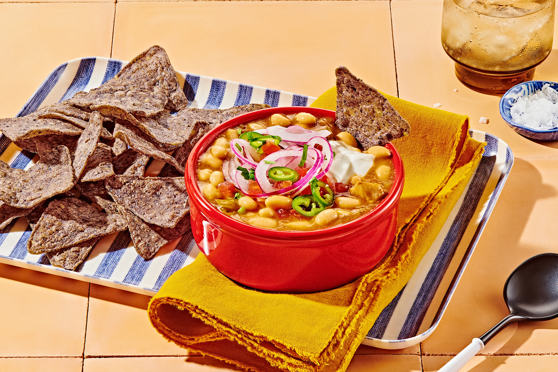Chicken chili with white beans and jalapenos in a red bowl with blue corn tortilla chips