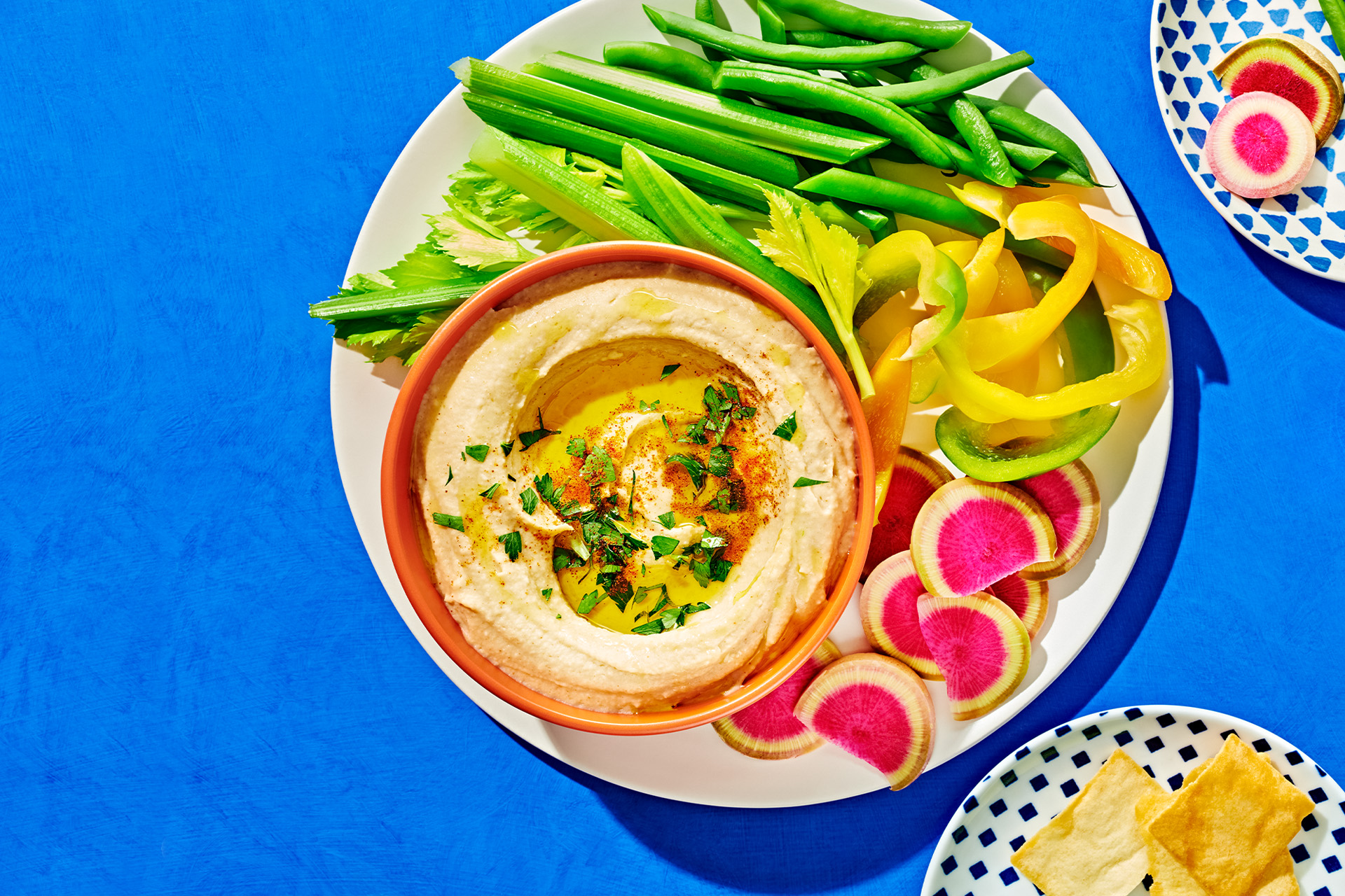 Close-up of hummus with olive oil and fresh herbs in an orange bowl