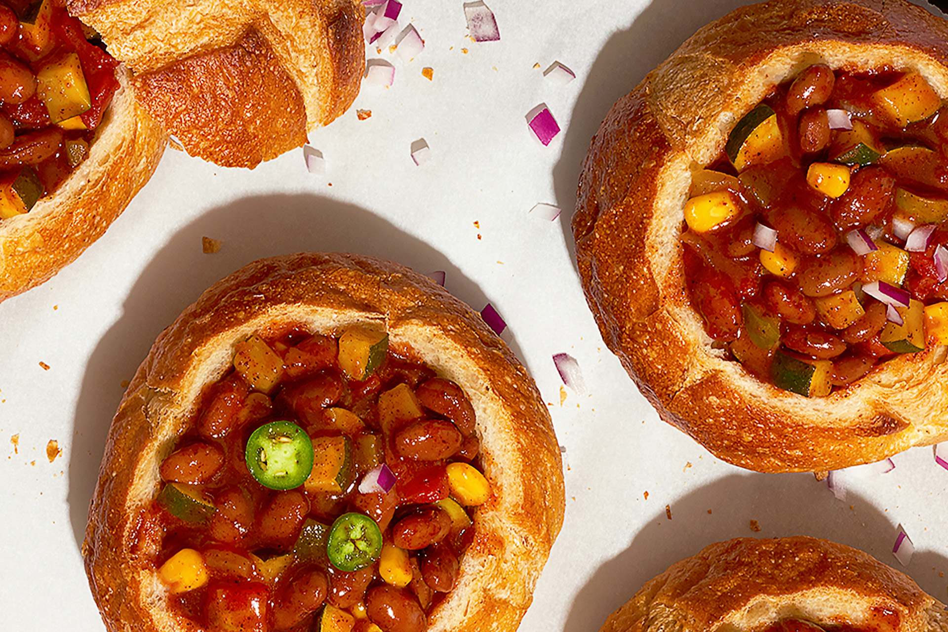 Five bread bowls on a baking sheet filled with vegetarian chili