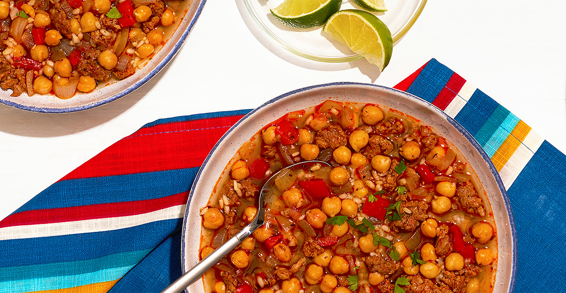 Chickpea and chorizo soup and spoon in bowl on striped tablecloth