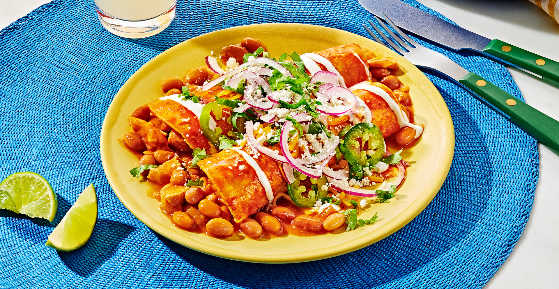Two bean and chicken enchiladas on a yellow plate, garnished with lime slices, onion and cilantro