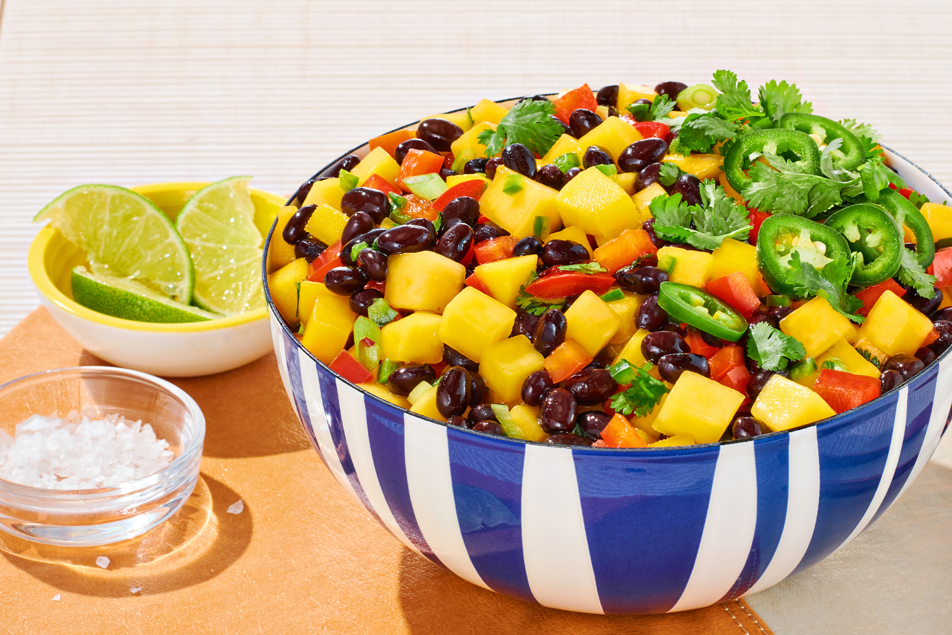 Black bean and mango salsa with lime wedges and salt in striped blue and white bowl