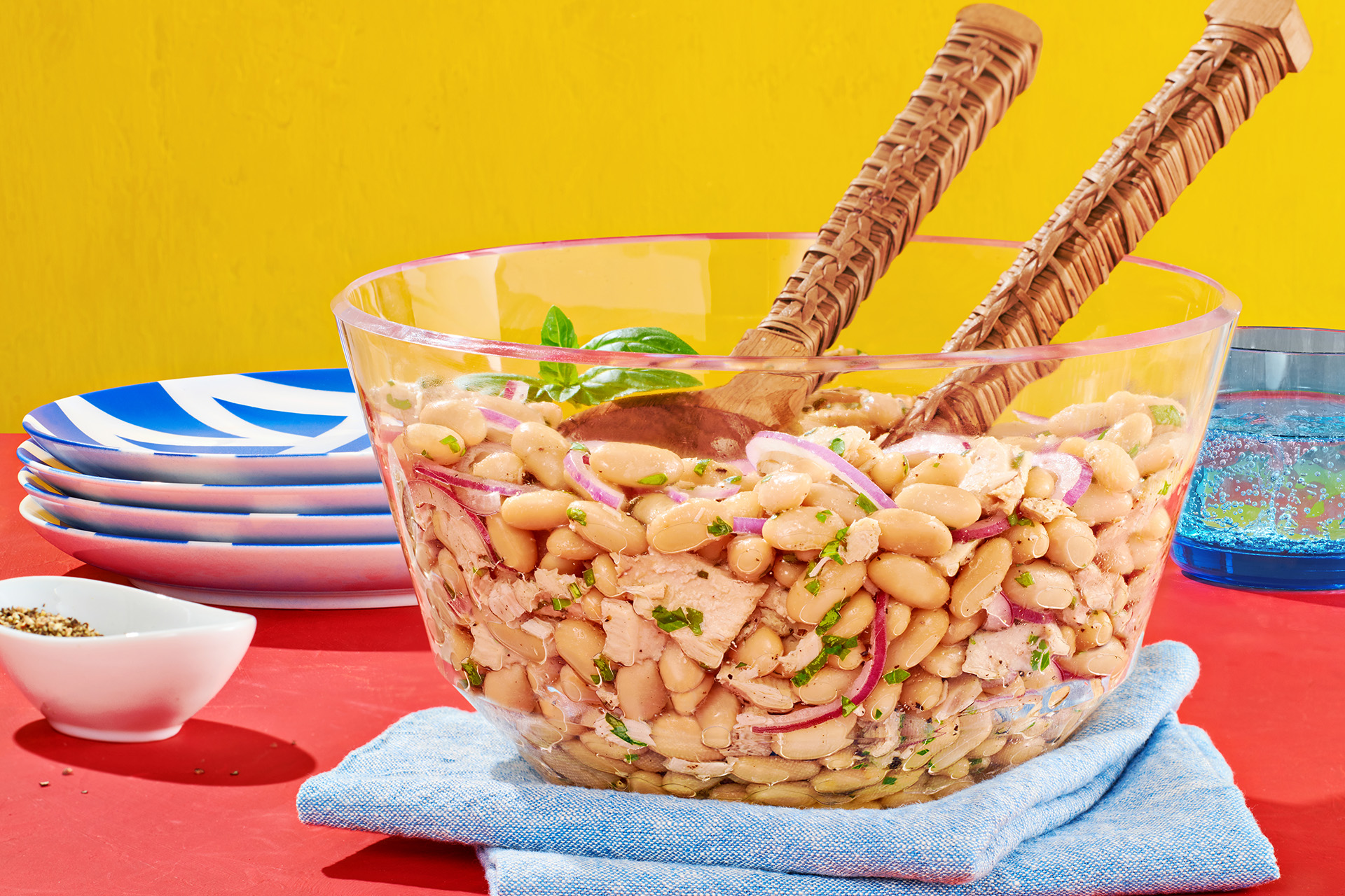 Tuna cannellini salad in a clear bowl with wooden serving spoons