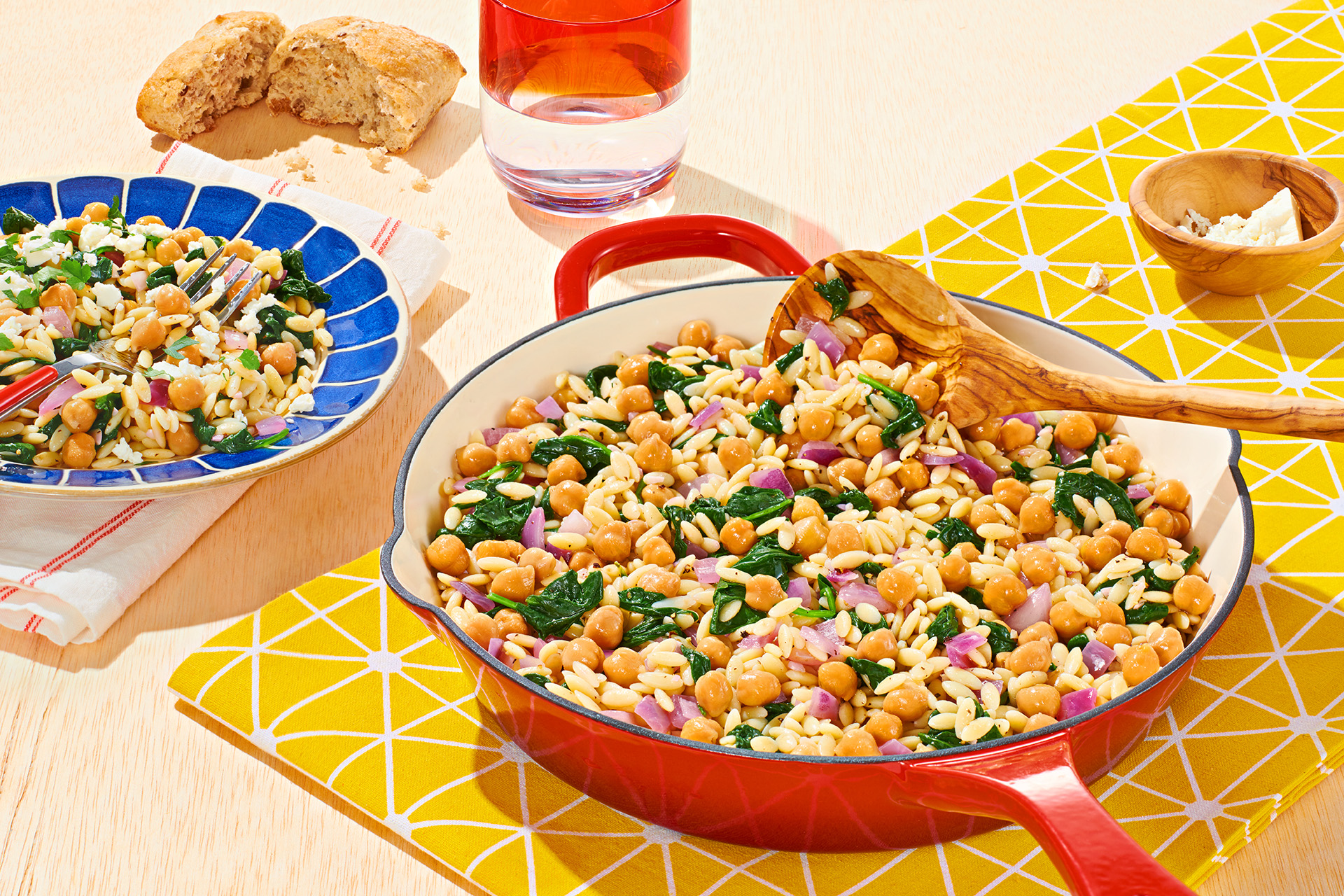 White enamel skillet filled with orzo, spinach and garbanzo beans, also known as chickpeas