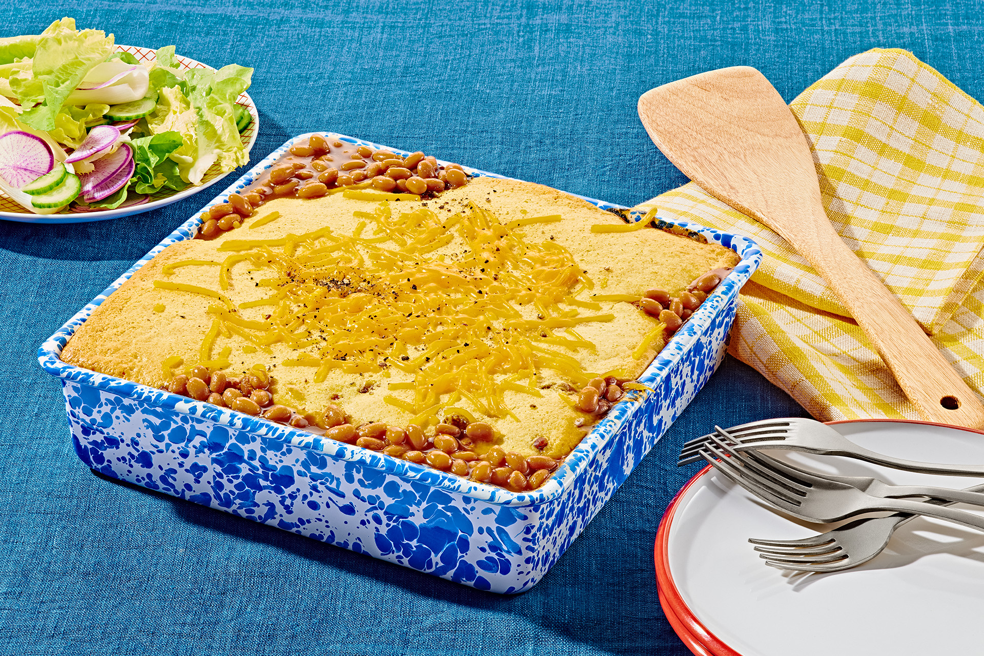 Baked bean, beef and cornbread casserole topped with melted cheese in square blue and white patterned baking dish