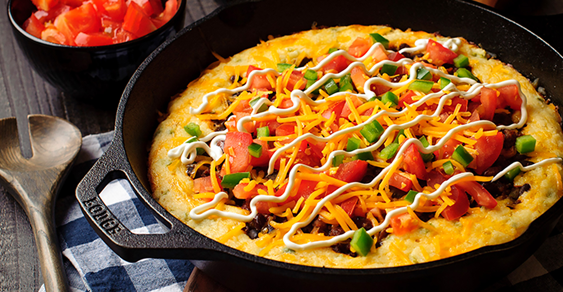 A cornbread and pinto bean skillet topped with tomatos and cheese in a cast iron skillet