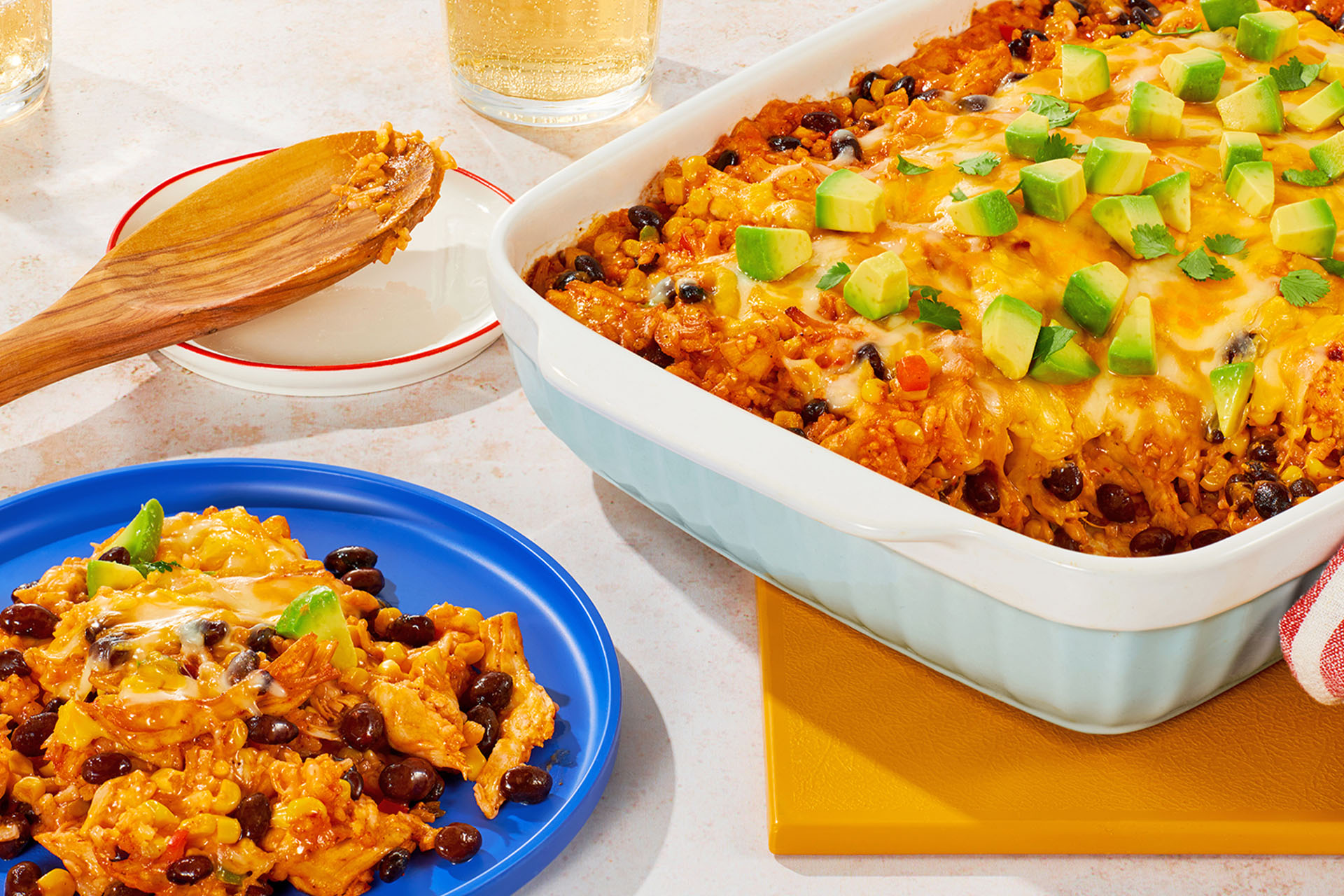 A casserole dish full of taco bake sitting next to a blue plate with a serving of the meal on it. 
