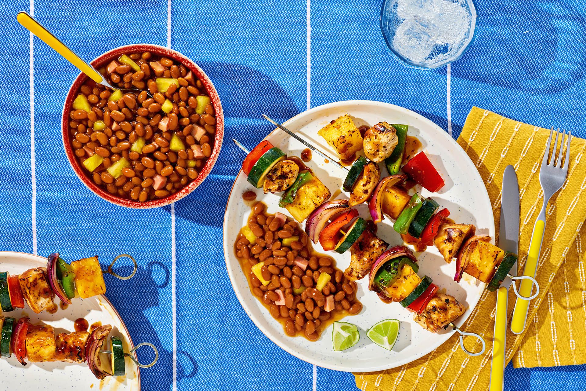A bowl of Hawaiian-style baked beans with pineapple and a platter of grilled kabobs.