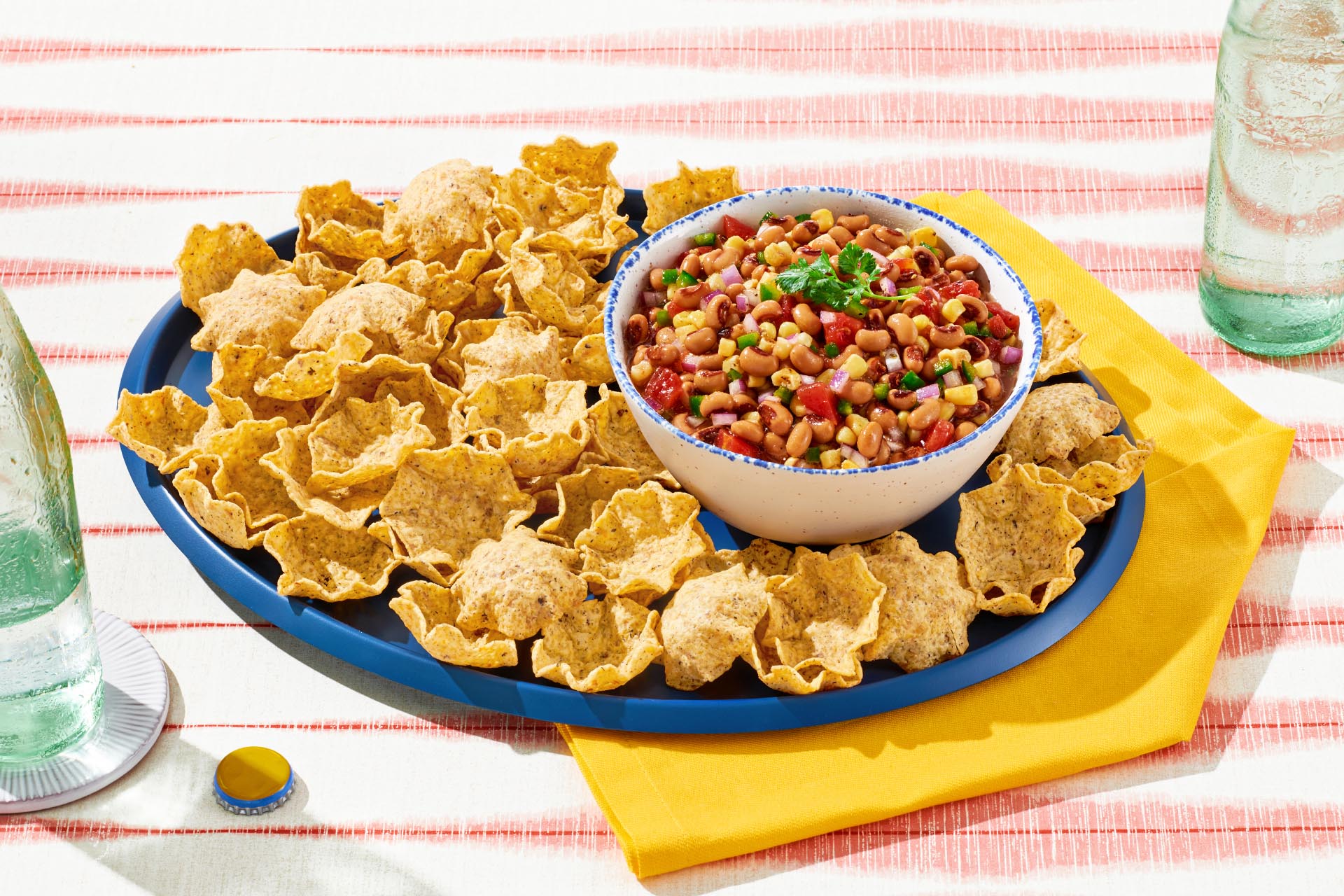 A bowl of black eye pea salsa on a blue plate of corn tortilla chips
