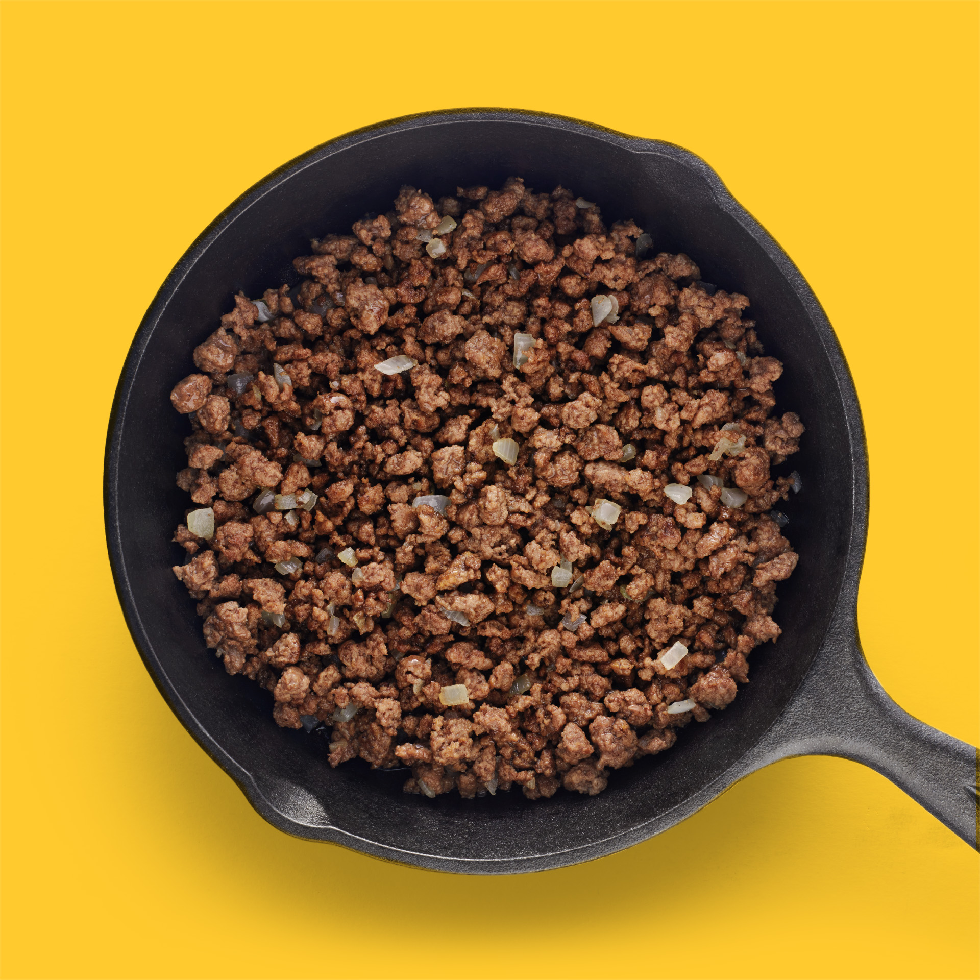 Cast iron pan full of browned ground beef with a yellow background.