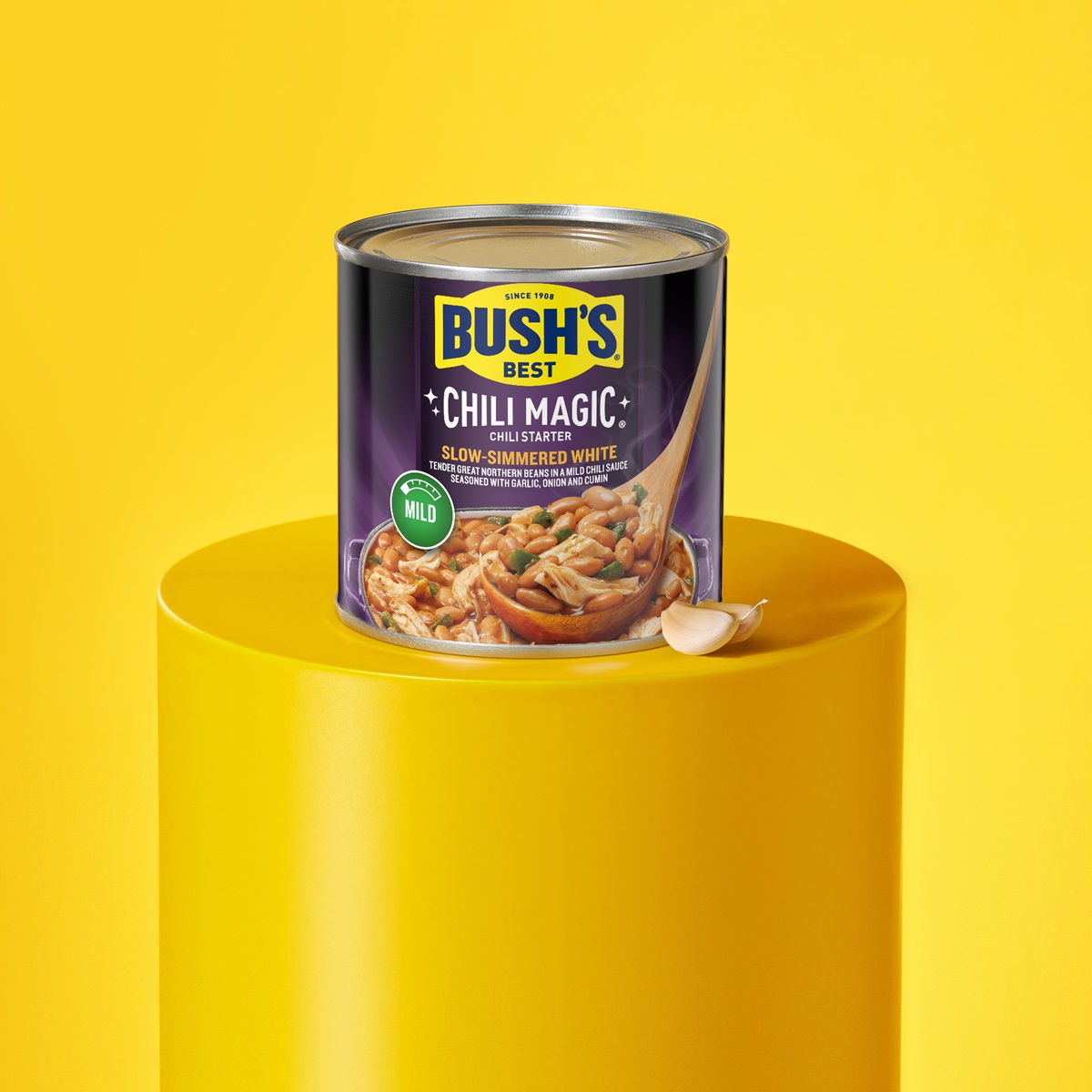 Can of Bush's Slow-Simmered White Chili Magic on a yellow pedestal with a clove of garlic.