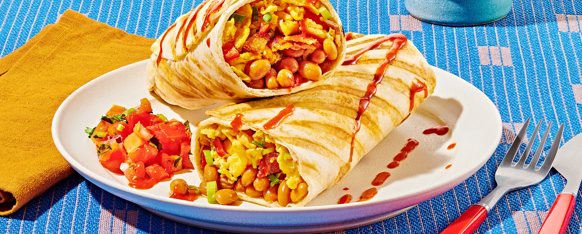 Grilled egg and bean breakfast burritos with bacon and tomato salsa on a white plate on a blue tablecloth