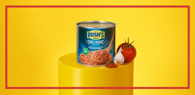 yellow pedestal with a can of Bush's Chili Magic, a tomato, garlic, and spices on top