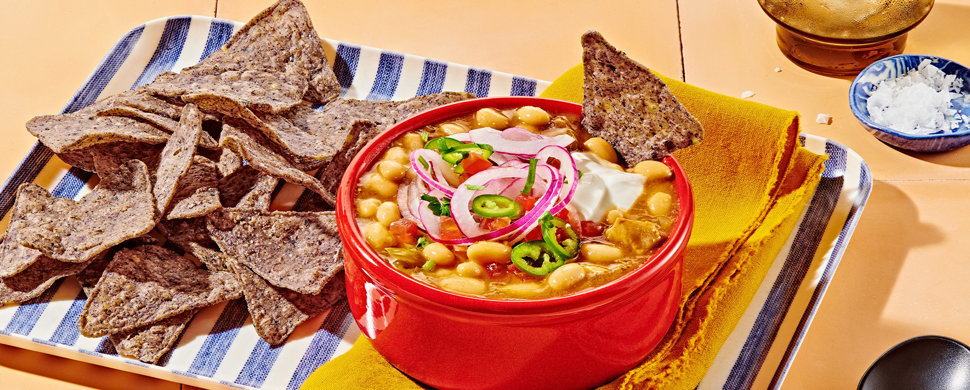 Chicken chili with white beans and jalapenos in a red bowl with blue corn tortilla chips