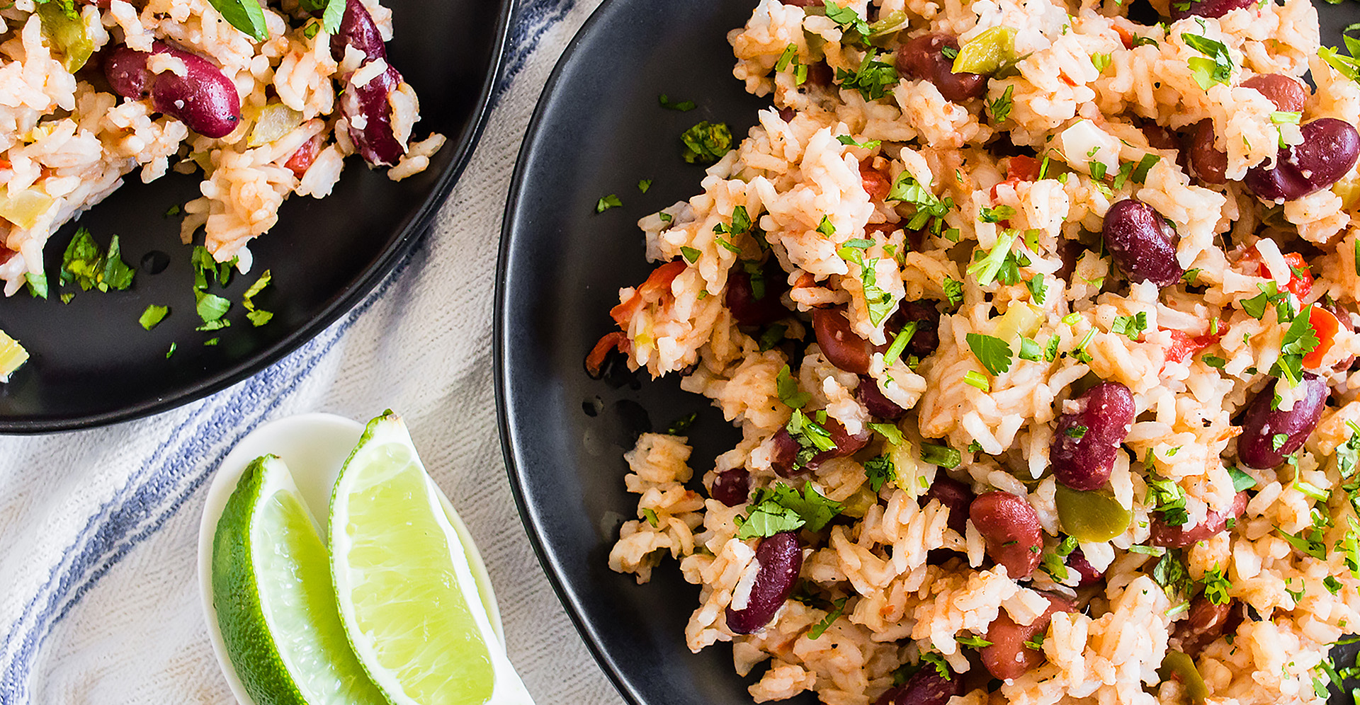 Red kidney beans and rice with lime wedges on two black plates on white tablecloth