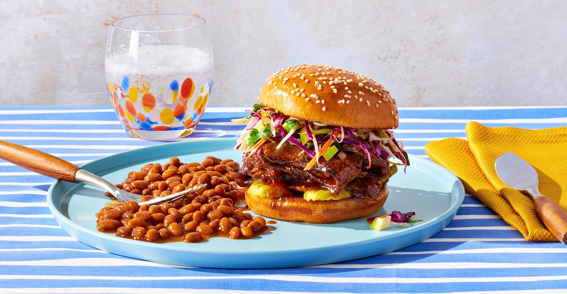 Barbecue beef brisket on a bun with a side of beans on a blue plate.