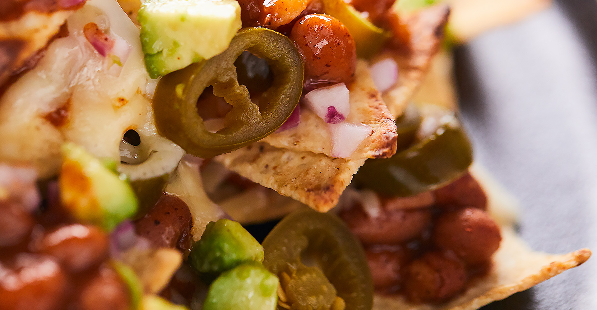 An extreme close-up of nachos with melted cheese, beans and sliced jalapenos