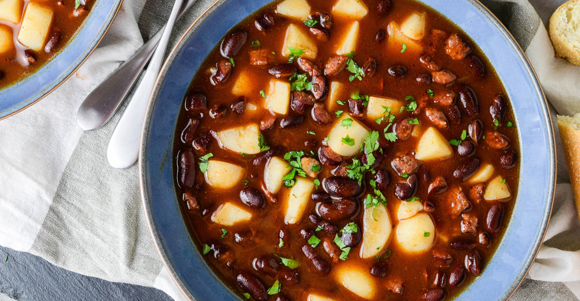 Spicy chili bean and potato chili garnished with cilantro in a blue bowl