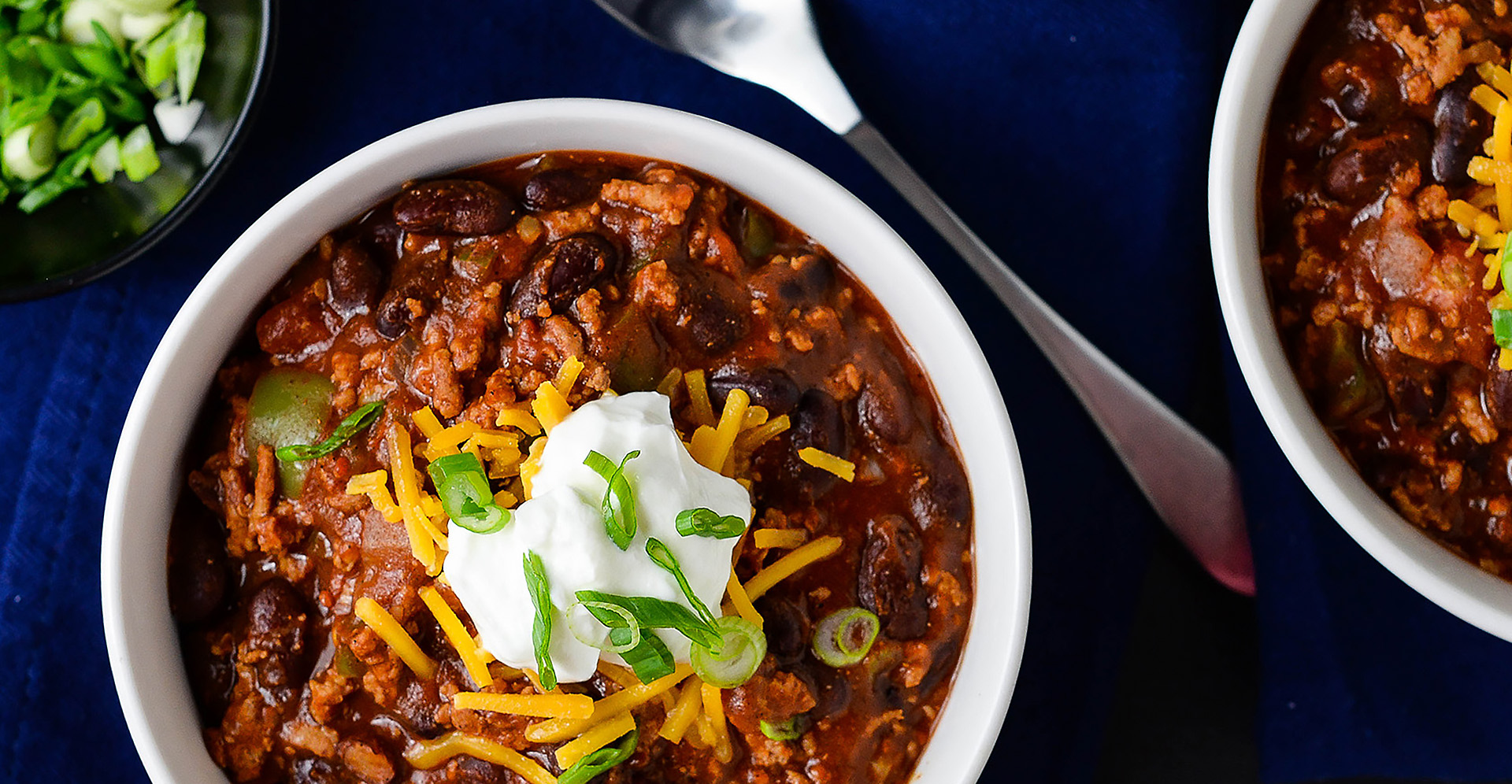 Beef and bean chili topped with sour cream and green onions in a white bowl