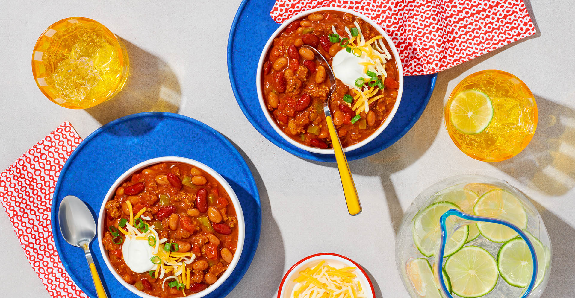 Two bowls of mixed chili beans chili in blue bowls with red napkins and refreshments.