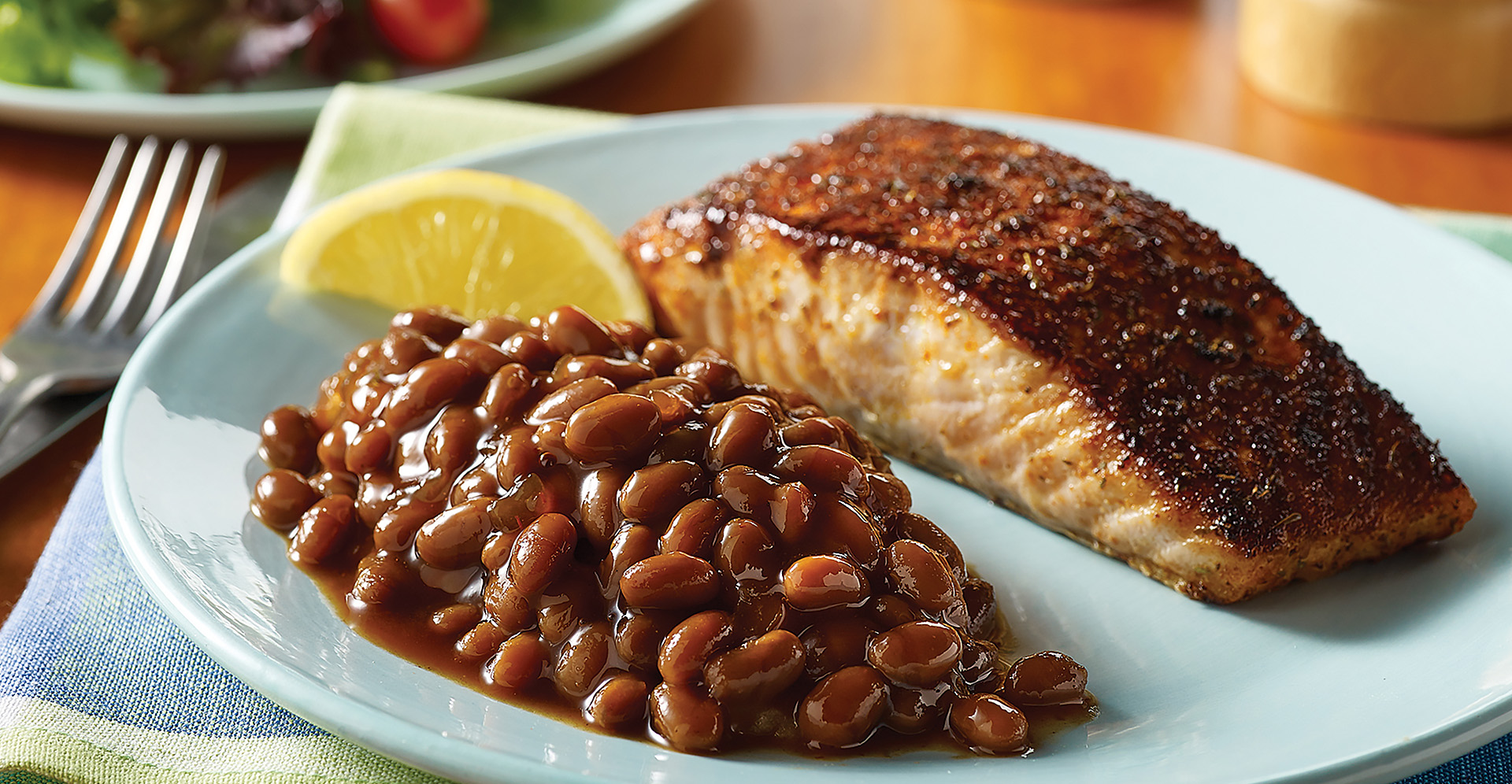 Blackend salmon with side of baked beans and a lemon slice on a white plate