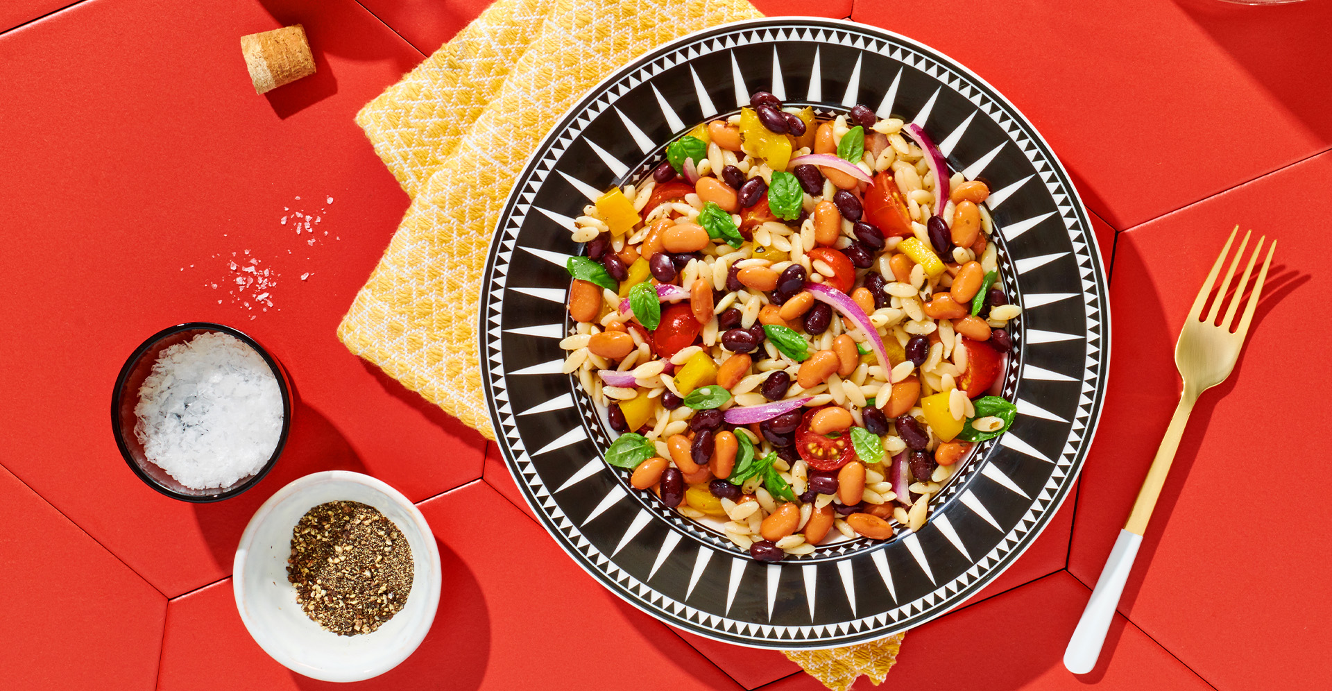 Mediterranean orzo, bean and tomato pasta salad in a black-and-white patterned bowl