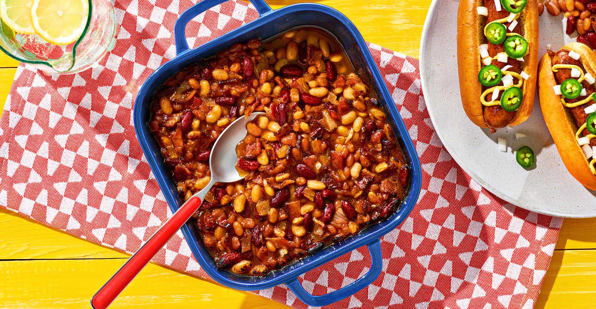 Baked Beans Casserole in a blue enamel dish atop a colorful napkin.